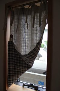 小窓に掛けられ、片方の裾をめくったチェック柄のカーテン