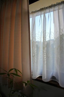 花の刺繍のカフェカーテンが掛かった窓の写真